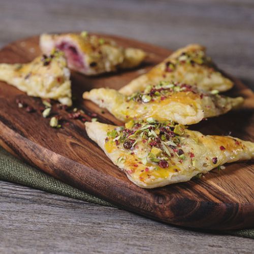 Puff pastry triangles filled with mortadella and caramelized onion, garnished with chopped pistachios and pink pepper